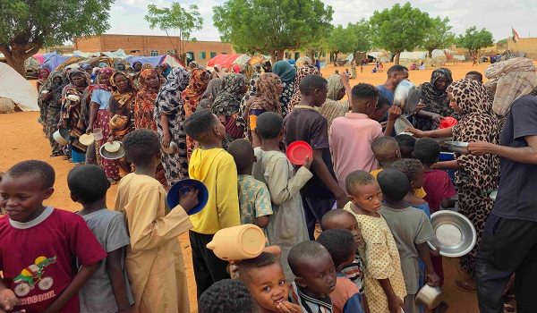 Women and children queue to receive free food being distributed in al-Mohayra camp for displaced people, near the city of El-Obeid in the southern Kordofan region, on June 29, 2026. El-Obeid, a city of half a million people that hosts nearly 100,000 refugees displaced by violence elsewhere, has, in recent weeks, faced its most intense RSF attacks yet. After breaking a prolonged siege in February last year, the army has struggled to stop the RSF from reimposing a blockade through repeated drone strikes targeting the city, its infrastructure and the main highway out. (Photo by AFP)
