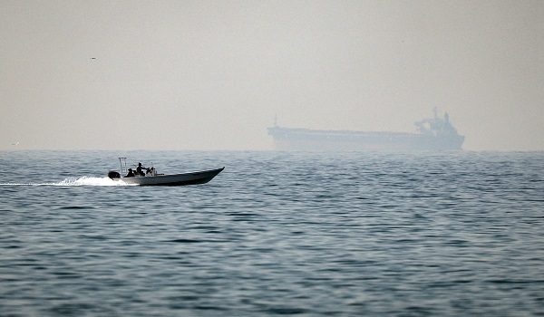 (FILES) A motorboat cruises along the shore off the town of Al Jeer on the Strait of Hormuz in the northern emirate of Ras Al Khaimah, with a tanker seen in the background, on February 25, 2026. The US president sent a peace plan to Iran as he voiced optimism on March 25, 2026 at ending nearly a month of warfare, with Tehran announcing that it will let "non-hostile" oil vessels go through the crucial Strait of Hormuz. Oil prices dropped sharply and stocks in Asia rose on broader de-escalation hopes following nearly four weeks of war, as the US president appeared to be ramping up efforts to bring an end to his joint military operation with Israel. (Photo by FADEL SENNA / AFP)