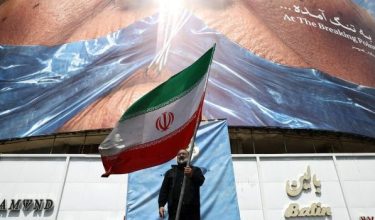 Seorang lelaki memegang bendera Iran berhampiran papan iklan anti-AS di Tehran/Foto REUTERS