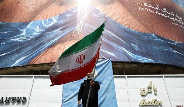 Seorang lelaki memegang bendera Iran berhampiran papan iklan anti-AS di Tehran/Foto REUTERS