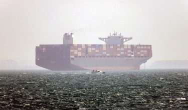 In this picture obtained from Iran's ISNA news agency and taken on May 2, 2026, the Iran-flagged container vessel Hamouna is pictured while anchored as a small motorboat passes by, in the Strait of Hormuz off Bandar Abbas in southern Iran. Iran's Revolutionary Guards on May 4 denied that any commercial ships had crossed the Strait of Hormuz, after the US military earlier said two US-flagged merchant vessels had transited through the vital waterway. (Photo by Amirhossein KHORGOOEI / ISNA / AFP) /