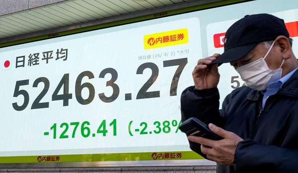 A man stands in front of an electronic quotation board displaying the closing numbers of the Nikkei Stock Average on the Tokyo Stock Exchange on a street in Tokyo on April 2, 2026. (Photo by Kazuhiro NOGI / AFP)