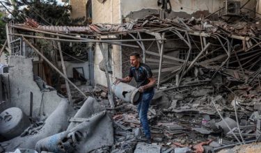 Seorang lelaki membawa tong gas memasak yang rosak di celah runtuhan bangunan yang musnah teruk selepas serangan Israel/Foto AFP