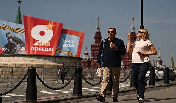 People eat ice cream while walking down a street with Victory Day decorations and Red Square in the background, in central Moscow on May 6, 2026. Russia will celebrate the 81st anniversary of the 1945 victory over Nazi Germany on May 9. (Photo by Igor IVANKO / AFP)