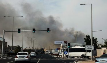 Motorists drive past a plume of smoke rising from a reported Iranian strike in the industrial district of Doha on March 1, 2026. AFP correspondents and residents heard fresh explosions across the Gulf cities of Dubai, Abu Dhabi, Doha and Manama on March 1, as Iran pressed on with its retaliatory campaign for a second day. (Photo by AFP)