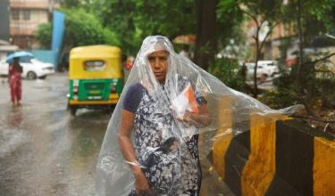 Seorang wanita berteduh dengan plastik ketika hujan lebat di New Delhi, India/Foto REUTERS