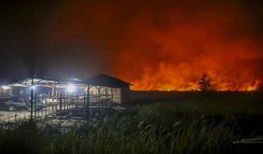 Flames and thick smoke glow against the night sky as a massive wildfire burns near residential structures in the Panarung area of Palangkaraya, Central Kalimantan province, on October 8, 2026. Toxic haze has shrouded parts of Indonesia, Malaysia and Singapore for weeks as Jakarta struggles to contain fires that have scorched large tracts of Borneo and Sumatra, with the smoke drifting across the region. (Photo by REINA / AFP)