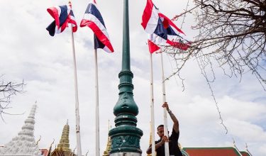 A worker displays flagpoles with Thailands national flag on a pavement opposite the main entrance gate to the Grand Palace complex in Bangkok on June 12, 2026. Thai Princess Bajrakitiyabha Mahidol, the king's eldest daughter, has died aged 47, the royal palace announced on June 12, more than three years after she was hospitalised following a sudden illness. (Photo by ANTHONY WALLACE / AFP)