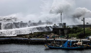 A fisherman handles a rope near a fishing boat as waves crash over a breakwater in Yilan on July 10, 2026, as Typhoon Bavi moves toward northeastern Taiwan. (Photo by I-Hwa Cheng / AFP)