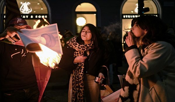 Anti-Iranian regime protesters light cigarettes with a lit paper depicting Ali Khamenei, Supreme Leader of Iran during a gathering outside the US Consulate in Milan, on January 13, 2026. (Photo by Piero CRUCIATTI / AFP)