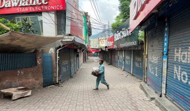 A man walks with his belongings along a closed market, during a shutter-down strike called by the recently banned Joint Awami Action Committee (JAAC), an alliance of civil society groups, in Muzaffarabad, Pakistani Kashmir, June 19, 2026. Picture taken with a mobile phone. REUTERS/Naseer ud Din