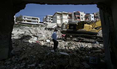 Mohammed Mawaadi, a Palestinian man living in Lebanon, stands by the damaged wall of his apartment as he looks at the rubble of a nearby building that was hit in January by an Israeli strike in the southern village of Qannarit, on February 16, 2026. Despite a November 2024 truce that sought to end more than a year of hostilities between Israel and Hezbollah, Israel has kept up regular strikes on Lebanon, usually saying it is targeting the Iran-backed group. (Photo by Joseph EID / AFP)