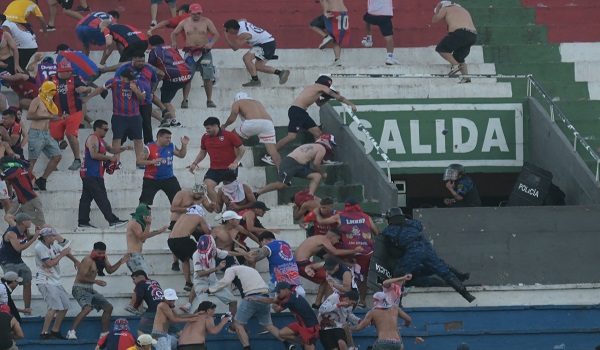 Fans of Cerro Porteno clash with police officers during the Paraguayan tournament football match between Olimpia and Cerro Porteno at the Defensores del Chaco stadium in Asuncion on April 19, 2026. Several people were injured and at least a hundred were arrested following incidents that occurred during the Paraguayan football derby between Olimpia and Cerro Porteno, which was suspended in the first half in Asuncion on April 19, 2026. (Photo by Daniel DUARTE / AFP)