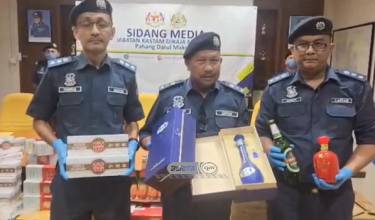 MOHD. ASRI (tengah) bersama minuman keras dan rokok yang dirampas dalam serbuan pada sidang akhbar di Bentong hari ini / Foto RTM