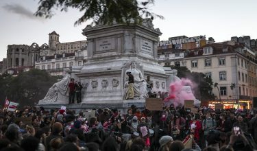 People gather holding flags and shouting slogans during a protest against housing shortage, soaring rents and low wages at Rossio square in Lisbon, on November 20, 2026. Thousands of people demonstrated today evening in Lisbon and other Portuguese cities, hours after police dismantled housing protest camps at dawn and arrested 55 people. (Photo by PATRICIA DE MELO MOREIRA / AFP)