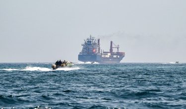 (FILES) A boat approaches the St Kitt's and Nevis-flagged container ship Marsa Victory while crusing in the waters of the Strait of Hormuz off the coast of Khasab in Omans northern Musandam peninsula on June 25, 2025. The US president sent a peace plan to Iran as he voiced optimism on March 25, 2026 at ending nearly a month of warfare, with Tehran announcing that it will let "non-hostile" oil vessels go through the crucial Strait of Hormuz. Oil prices dropped sharply and stocks in Asia rose on broader de-escalation hopes following nearly four weeks of war, as the US president appeared to be ramping up efforts to bring an end to his joint military operation with Israel. (Photo by Giuseppe CACACE / AFP)