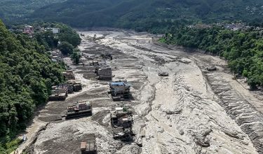 Houses lie partially submerged in muddy water along a riverside after flash floods at Trishuli Bazar in Nepal's Nuwakot district on August 26, 2026. A massive flood swept through Nepal's northern Rasuwa district on August 26, damaging roads and power infrastructure as authorities scrambled to assess the scale of the destruction. (Photo by Prabin RANABHAT / AFP)