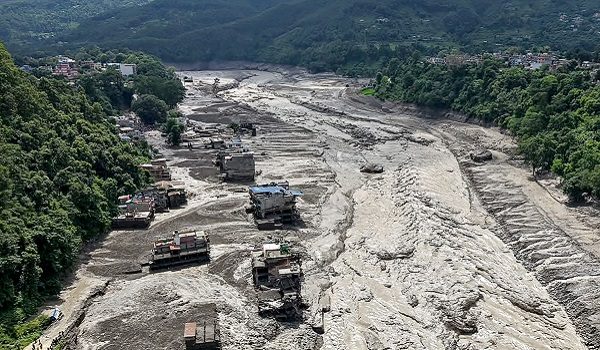 Houses lie partially submerged in muddy water along a riverside after flash floods at Trishuli Bazar in Nepal's Nuwakot district on August 26, 2026. A massive flood swept through Nepal's northern Rasuwa district on August 26, damaging roads and power infrastructure as authorities scrambled to assess the scale of the destruction. (Photo by Prabin RANABHAT / AFP)