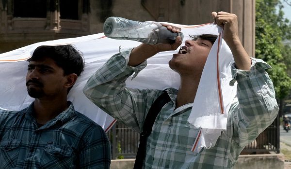 Men cover their heads with a scarf as they drink water on a hot afternoon, along a street in Amritsar on April 27, 2026. (Photo by Narinder NANU / AFP)