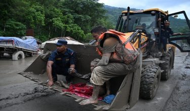 Rescue personnel use an excavator to carry a person affected by flash floods at Devghat in Nepal's Nuwakot district on August 26, 2026. Massive flooding killed eight people in Nepal on August 26, as Chinese state media reported "major casualties" from a mudslide at a Tibet trade hub on China's side of the nations' shared border. (Photo by Prakash MATHEMA / AFP)