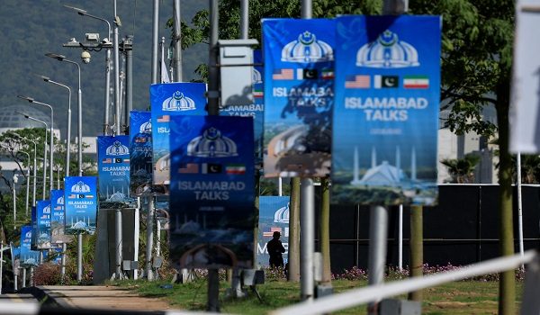 A silhouetted man stands next to advertisement posters reading “Islamabad Talks” at the Convention Centre, as Pakistan prepares to host the U.S. and Iran for the second phase of peace talks in Islamabad, Pakistan April 22, 2026. REUTERS/Akhtar Soomro