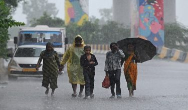 People walk along a street during rainfall in New Delhi on July 28, 2026. (Photo by Arun SANKAR / AFP)