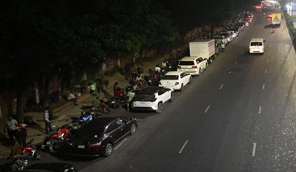 People queue up along a road, to refuel their vehicles at a filling station in Dhaka on April 21, 2026 amid Bangladesh's fuel crisis triggered by the Middle East war. (Photo by MUNIR UZ ZAMAN / AFP)